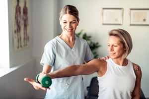 Physical Therapist Assistant helping a female patient lift weights